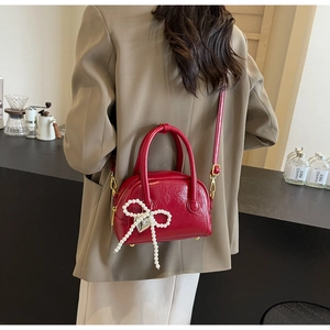 Détail du sac à main rouge avec nœud en perles et pendentif cœur argenté sur le modèle