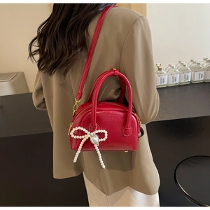 Détail d'un sac coquillage rouge en similicuir avec nœud en perles et pendentif cœur