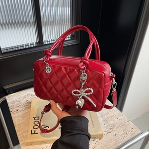 Chic red quilted crossbody mini bag with silver bow and heart charm on marble surface