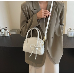 Détail du sac coquillage blanc en cuir avec nœud perlé et pendentif en cœur