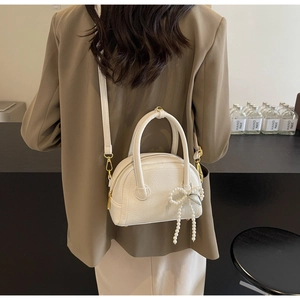 Vue détaillée du sac coquillage blanc avec nœud en perles porté sur un blazer