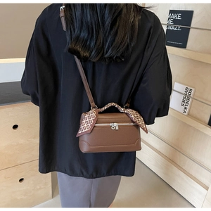 Close-up of brown lychee leather handbag with decorative printed silk scarf on handle