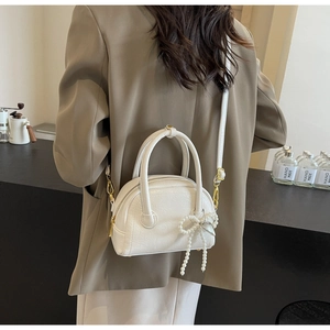 Détail d'un sac bowling blanc avec nœud en perles et fermetures éclair dorées sur modèle