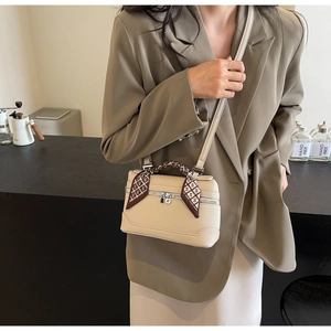 Close-up of beige leather box bag with brown silk scarf wrapped around the top handle