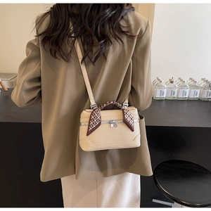 Detail of a beige leather crossbody bag with an elegant silk scarf wrapped on the handle