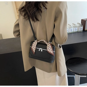 Detail of black leather handbag featuring a silk scarf wrapped handle and slim strap