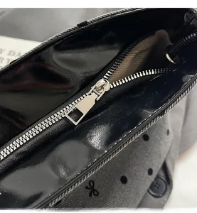 Détail du zip argenté sur sac noir brillant avec doublure en tissu à chevrons à pois