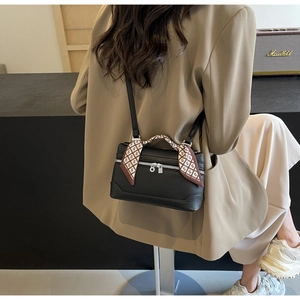 Detail of black pebbled leather box bag with decorative silk scarf on handle