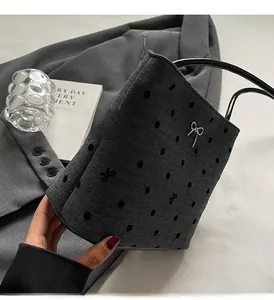 Détail d'un sac seau tissé gris à pois avec un nœud argenté sur fond de blazer chic