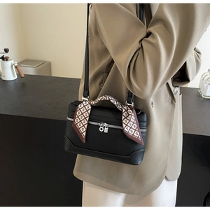 Detail of black pebbled leather crossbody bag with silk scarf wrapped handle and zippers