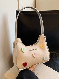 Beige contrast underarm bag with colorful heart patches on a sleek black background