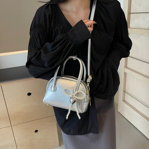 Mini sac Boston argenté avec nœud en perles et breloque cœur porté par un mannequin chic