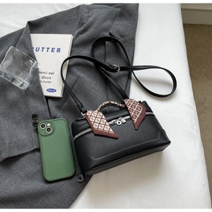 Detail of black lychee leather handbag with silk scarf handle on grey blazer background