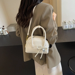 Petit sac bowling blanc avec nœud en perles et pendentif cœur sur comptoir moderne