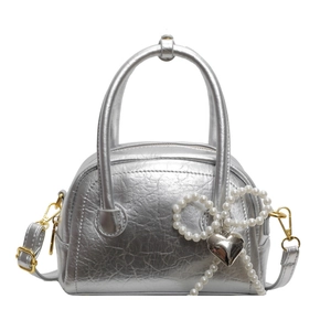 Sac coquille en cuir argenté avec nœud en perles et pendentif cœur sur fond blanc