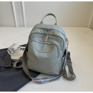 Détail du sac à dos en similicuir gris-vert avec fermetures éclair argentées sur lit