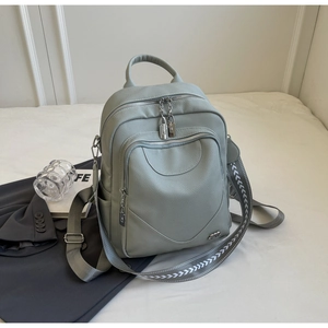 Détail du sac à dos en cuir gris clair avec bandoulière tissée sur surface blanche