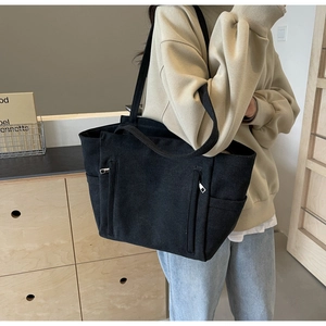 Lifestyle view of a black canvas tote bag with metal zippers shown on a shoulder