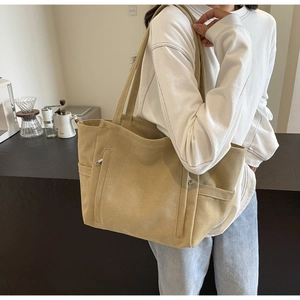 Detail of a large khaki canvas tote bag with wide shoulder straps and functional pockets