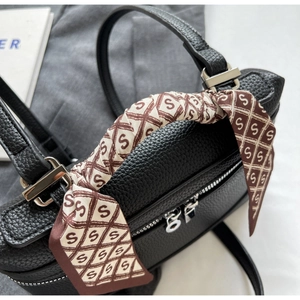 Close-up of black lychee leather handbag with silver zipper and silk scarf wrapped handle