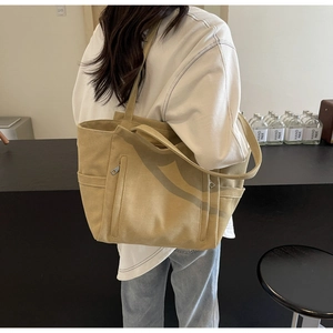 Detailed shot of khaki canvas tote bag featuring dual front zipper pockets and side slots