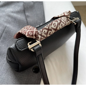 Close-up of black lychee grain leather bag with decorative printed silk scarf on handle