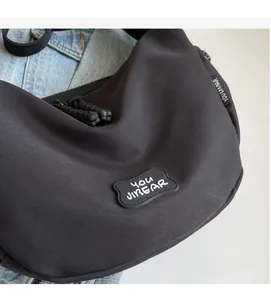 Détail du sac hobo noir montrant le patch logo en silicone et la tirette de zip tissée