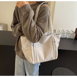 Detail of cream canvas tote bag showing front zipper pocket and wide shoulder straps