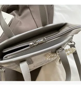 Detail of smooth silver zipper and pearl bow charm on a grey textured bucket bag