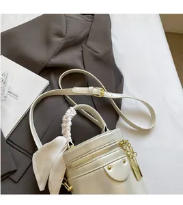 Detail of cream bucket bag featuring woven handle, decorative scarf and metal charm