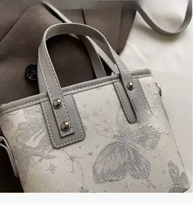 Detailed view of silver butterfly embroidery and rivets on fabric bucket bag