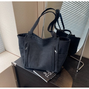 Detailed view of black canvas tote bag featuring functional front zipper pockets