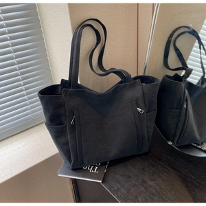 Detail of large black canvas tote bag featuring side pockets and symmetric zippers