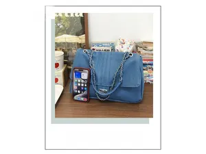 Détail du sac bandoulière en denim avec chaîne, montrant la taille face au smartphone
