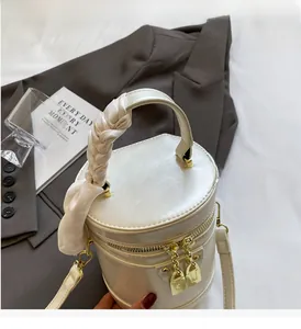 Detail of cream barrel bag featuring silk scarf handle and golden lock hardware