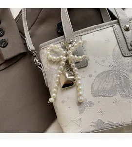 Detail of cream bucket bag with silver butterfly print and pearl bow charm accessory