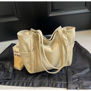 Detailed view of beige canvas tote bag with functional zippers and side pockets