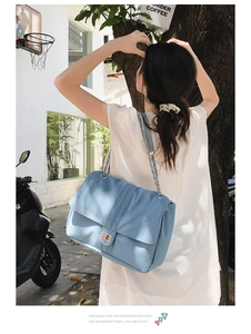 Détail du sac bandoulière en denim bleu clair avec chaîne dorée et fermoir pivotant chic