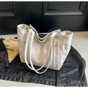Detailed view of white canvas tote bag with front zipper and side pocket on leather texture