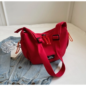 Détail d'un sac bandoulière en toile rouge avec logo et tirette de zip tissée décorative