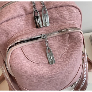 Détail du sac à dos en cuir rose avec fermetures éclair argentées et sangle à motifs