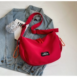 Détail du sac bandoulière rouge en nylon avec sangle réglable et écusson de marque