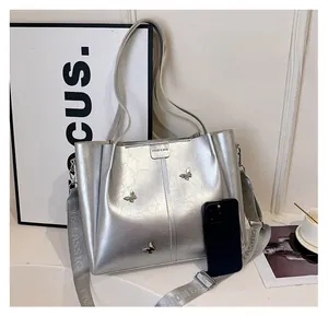 Detail of silver tote bag with metallic butterfly and wide strap showing interior capacity