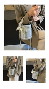 Detail of silver cylindrical bucket bag with woven handle and decorative floral silk scarf