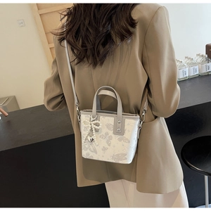 Detail of cream bucket bag with butterfly print, pearl bow charm, and metal strap link