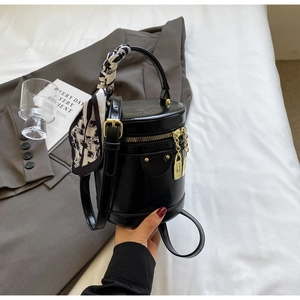 Detail of black cylinder bucket bag with gold hardware and silk scarf accent