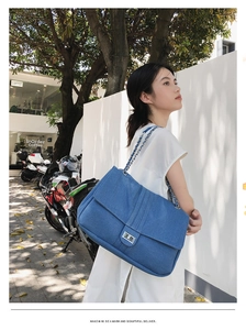 Détail d'un sac à épaule en jean bleu avec fermoir rotatif argenté et bandoulière chaîne