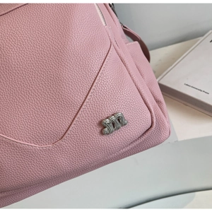 Détail de la texture cuir rose grainé et du logo métallique argenté en forme de M