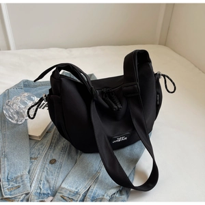 Détail du sac à bandoulière noir en toile avec sangle réglable posé sur une veste en jean