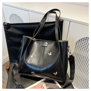 Macro detail of black oil wax leather tote bag featuring silver butterfly metal accents